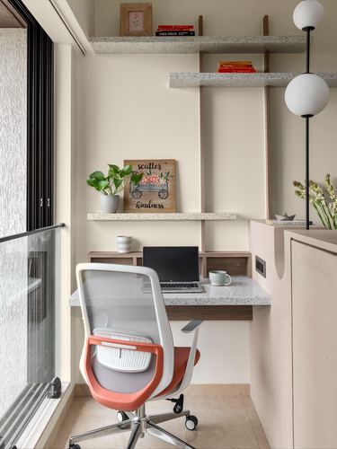 Small home office nook with terrazzo desk, floating shelves, and orange ergonomic chair by a window