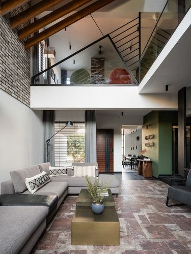 Double-height living room with brick wall, exposed beams, mezzanine, stone floor, grey sectional and brass table