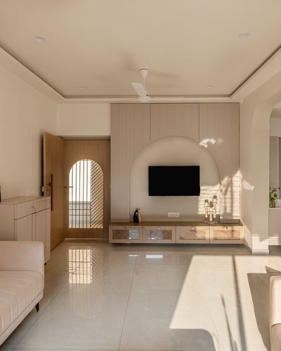Beige living room with fluted TV wall, arched niche, cane-front console, and arched wooden door letting in sunlight.