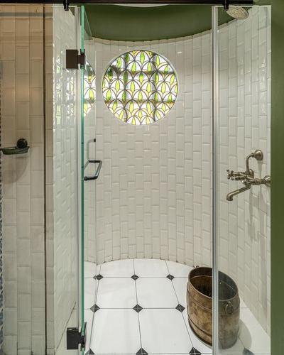 Curved white-tiled shower with circular stained glass window and glass door