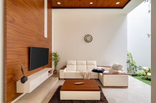 Minimalist living room with wood-panelled wall, cream sectional sofa, and view to a courtyard garden