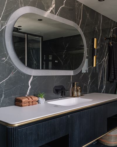 Dark marble bathroom vanity with oval ribbed mirror, brass trim, and black fluted cabinetry