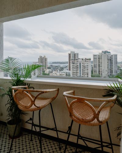 Two cane bar stools on a high-rise balcony overlooking Mumbai skyline under cloudy sky