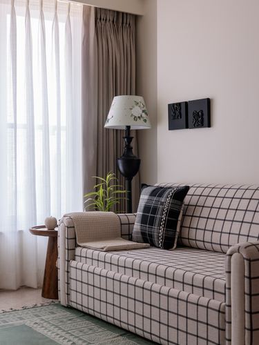 Corner of living room with checkered sofa, floral-shade floor lamp, sheer curtains, small black wall art