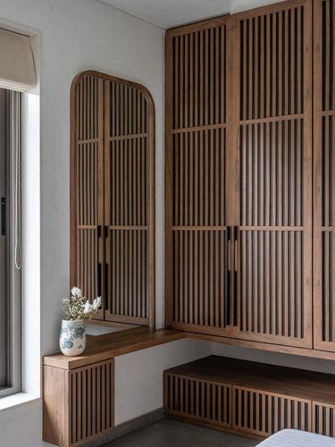 Fluted wood wardrobe with arched mirror and floating bench in a minimalist bedroom corner