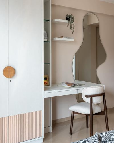 White wardrobe with wooden handle beside a dressing table with an amoeba-shaped mirror