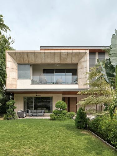 Two-storey contemporary villa facade with cantilevered stone volume, balcony, and landscaped lawn