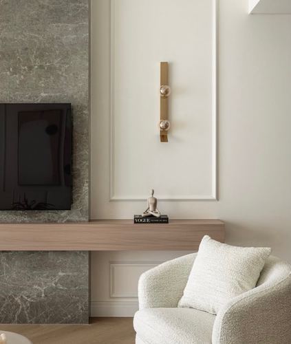 Living room corner with stone tv wall, wood console, brass sconce, and boucle armchair