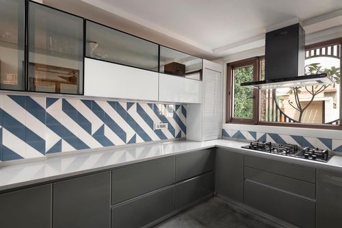 L-shaped kitchen with grey cabinets, blue-white geometric backsplash and black chimney hood