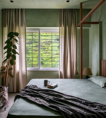Sage-green bedroom with lime-plaster walls, wooden four-poster frame, and a garden-view window