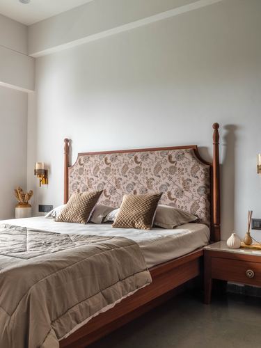Four-poster wood bed with floral-print headboard and beige linens against a plain grey wall