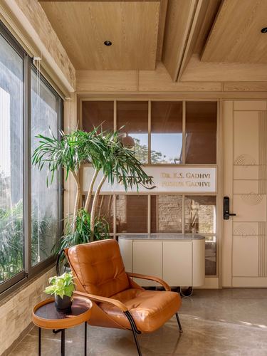 Foyer with tan leather chair, palm plant, and wood-framed glass wall with nameplate
