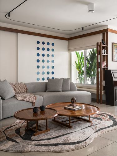 Grey L-shaped sofa with round wood coffee tables and blue ceramic disc wall art in a Hyderabad apartment living room