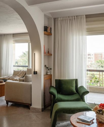 Living room with arched doorway, green velvet armchair, and sheer curtains beside a balcony view