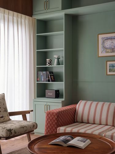 Sage green living room niche with built-in bookshelf, striped sofa, and framed art