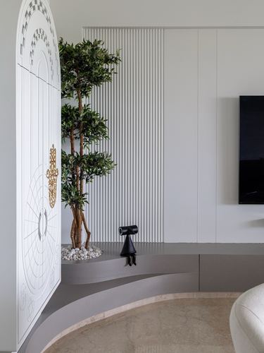 Arched mandir door beside fluted white panelling and a potted tree in a curved foyer