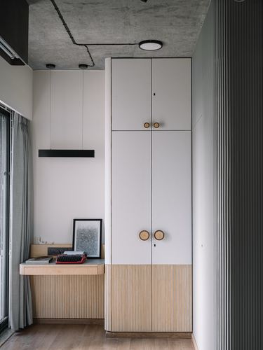 White wardrobe with round wooden handles beside a study nook under exposed concrete ceiling