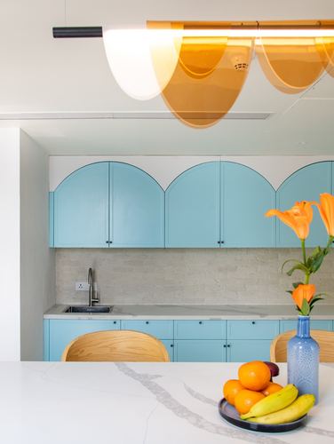 Blue arched kitchen cabinets with amber pendant light and citrus fruit on marble counter