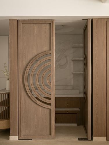Wooden pivot door carved with concentric arches opens to a marble pooja niche with om motif