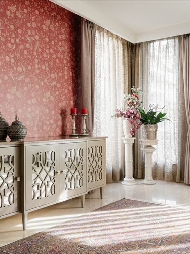 Foyer with fretwork mirrored cabinet, floral wallpaper, sheer curtains and pedestal urns on marble floor
