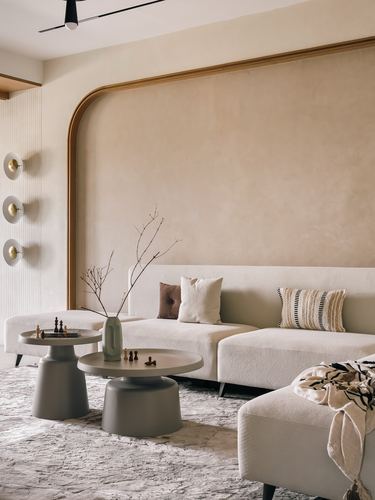 Beige living room with curved arched wall, boucle sofa, and round grey pedestal side tables