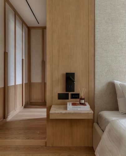 Wood-panelled bedroom nook with cantilevered stone nightstand and black wall sconce beside upholstered bed