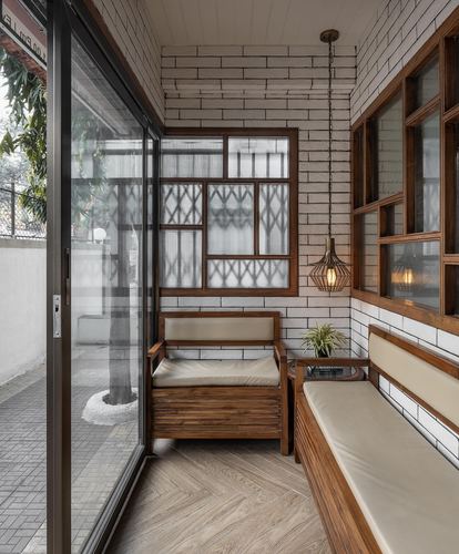 Narrow balcony seating nook with wooden bench, lattice window, and hanging lanterns against white brick wall