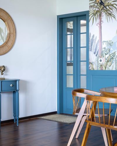 Foyer with teal door, round rattan mirror, blue console table, and tropical mural wall