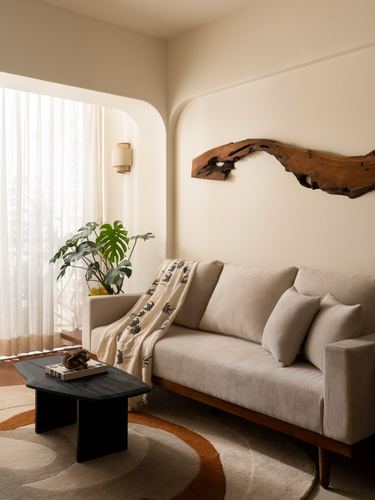 Beige sofa in arched niche beneath a driftwood wall sculpture, black coffee table on round rug