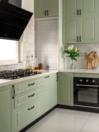 Sage green kitchen corner with black chimney hood, oven, and stone countertop