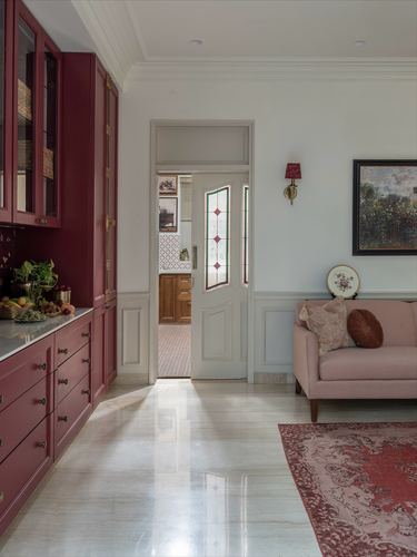 Maroon kitchen cabinetry beside a doorway leading to a pink sofa living area