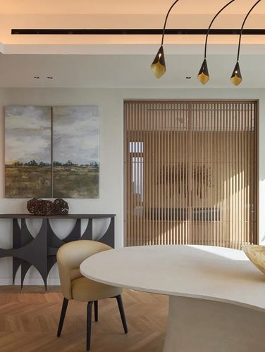 Dining nook with curved stone table, mustard chair, and wood-slatted sliding doors in Dubai apartment
