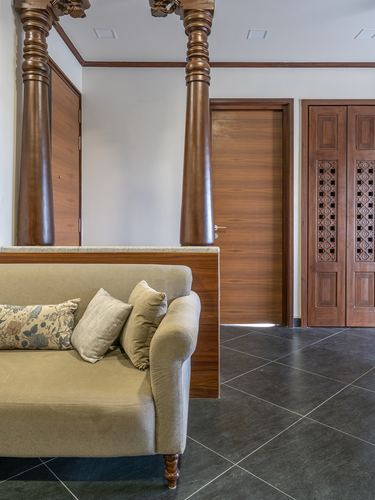 Living room corner with carved wooden pillars, beige sofa, and jaali-patterned wooden door