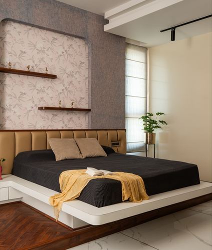 Bedroom with tufted tan headboard, platform bed, floral wallpaper niche and wood shelves with figurines