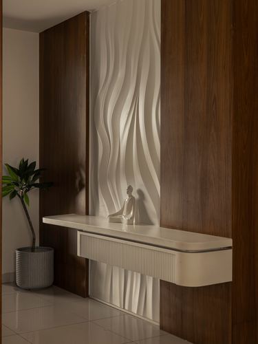Wooden panelled foyer wall with sculptural wave-textured niche, seated figurine, and floating stone console shelf