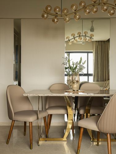 Beige dining room with marble table, brass legs, cane-globe chandelier, and mirrored wall reflecting living room