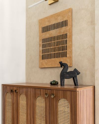 Wood and cane sideboard below a textile artwork and carved horse figurine on plaster wall