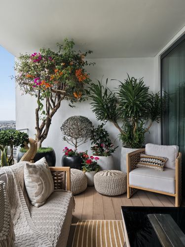 Balcony lounge with cane armchair, woven poufs and a flowering bougainvillea tree against city view