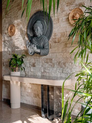 Foyer with stacked stone wall, Buddha relief, woven discs, and a curved-leg console table with plants