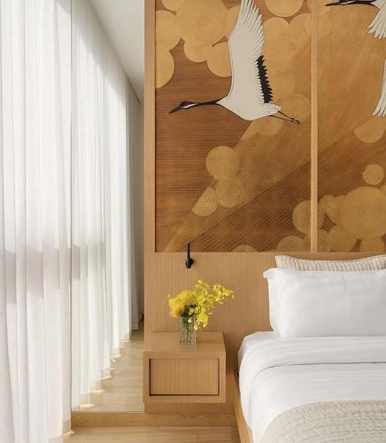 Bedroom with white bedding, sheer curtains, wood nightstand and crane-patterned wallpaper panel above headboard