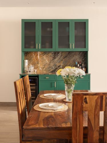 Green dining cabinetry with stone backsplash behind a wooden dining table set with placemats and flowers