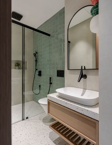 Bathroom with green scalloped tile shower, terrazzo floor, arched mirror, and wood vanity with vessel sink
