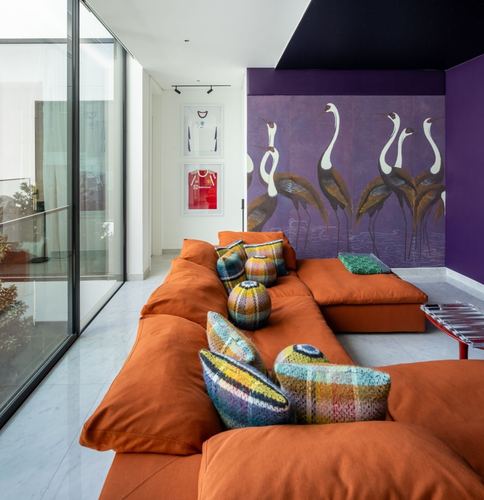 Orange modular sofa with knitted cushions against a purple crane mural wall