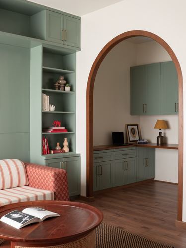 Sage green built-ins beside a wood-arched doorway opening to a small study nook