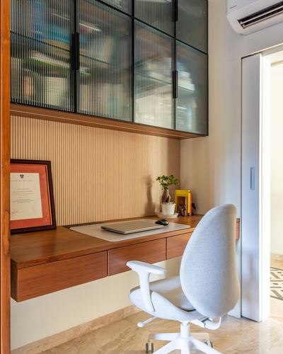 Floating wood desk under fluted glass cabinet with white ergonomic chair and framed certificate