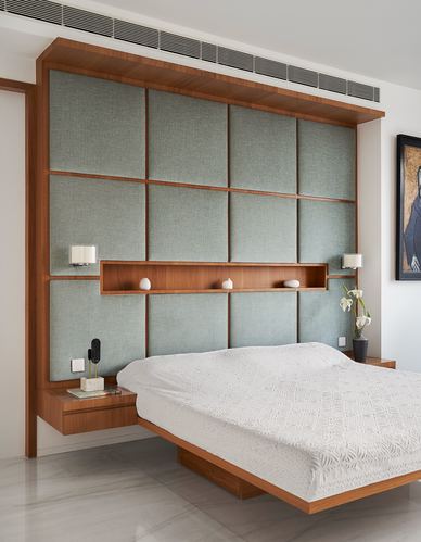 Bedroom with cantilevered bed against a wood-framed quilted headboard wall and stone floor