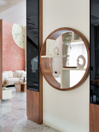 Round walnut-framed mirror on cream wall opens view to living room with brick wall beyond