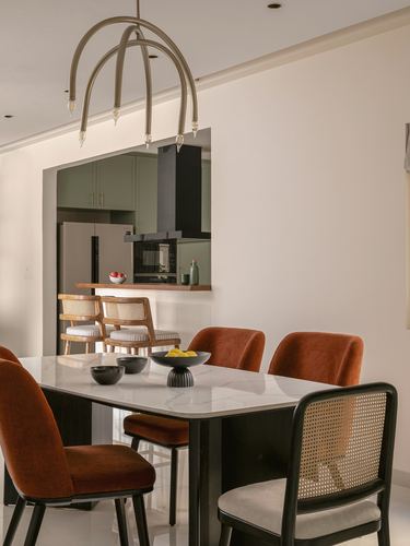 Dining table with rust velvet and cane chairs under arched pendant light, kitchen visible beyond