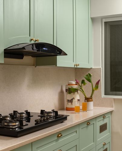 Sage green kitchen cabinets with black gas hob, chimney hood, and decorative jar on cream countertop