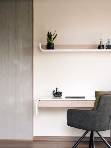 Minimalist wall niche with floating wood shelf, small desk, plant, figurines and grey leather chair
